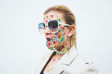 Woman with multi colored stickers on face and necklace in mouth against white background
