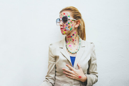 Woman with colorful stickers on face wearing sunglasses in front of white background