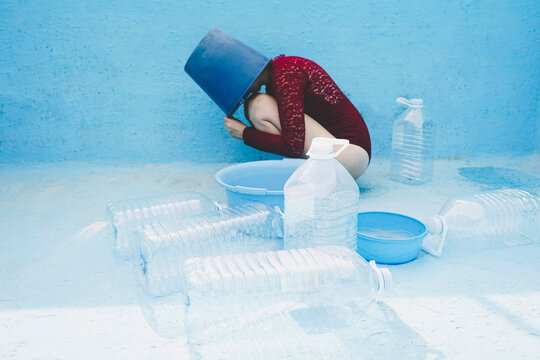 Woman with head inside bucket by plastic bottles in empty swimming pool