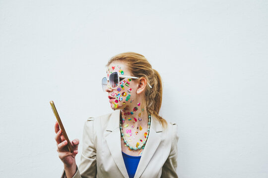 Woman with stickers on face using mobile phone in front of white background