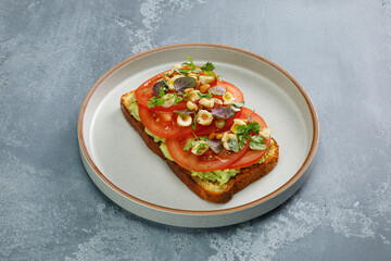 Toast with guacamole and slices of fresh tomatoes with fried hazelnuts on top. Vegetarian cuisine