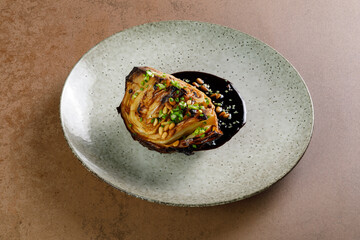 Grilled cabbage served with sauce and pine nuts. Delicious vegetarian food. Dark moody style.