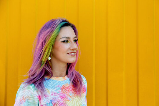 Smiling young woman with colorful hair in front of yellow wall
