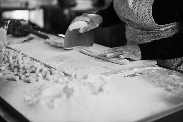 Woman preparing dough for gnocchi inside pasta factory - Soft focus on right hand - Black and white...