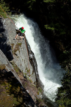 A young man rappels down a cliff next to a waterfall in Idaho.