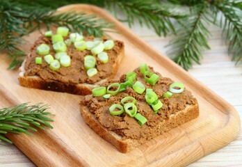 Pate spread from deer meat on whole grain bread  and green onion. Sandwich with meat pate on cutting board, decorated with spruce branch.