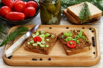Pate spread from deer meat on whole grain bread  and green onion. Sandwich with meat pate on cutting board, fresh tomatoes and spices for venison around. Decorated with spruce branch.