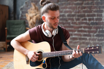 Handsome young man playing acoustic guitar sitting floor living loft room