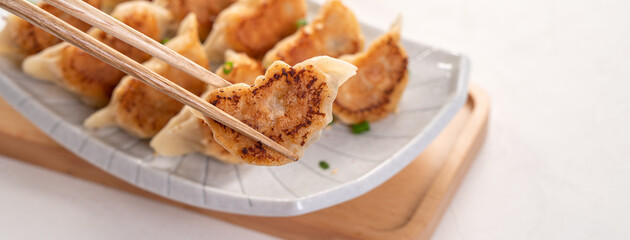 Pan-fried gyoza dumpling jiaozi in a plate with soy sauce on white table background.