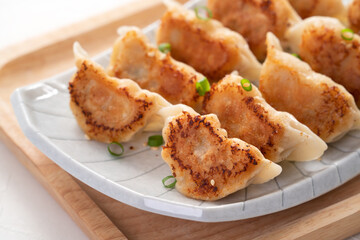 Pan-fried gyoza dumpling jiaozi in a plate with soy sauce on white table background.