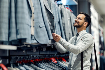 A happy man is picking new suit in a boutique.