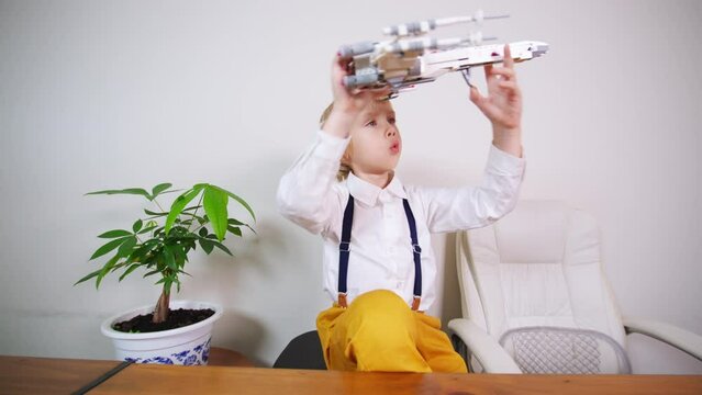 Blonde caucasian boy in white shirt and orange trousers plays with Star Wars spaceship model, a vessel designed for interstellar travel, specifically between star systems