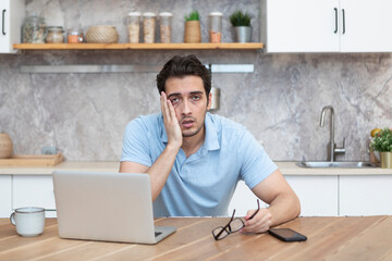 Stressed man working on laptop in the kitchen at home. Distance work concept	