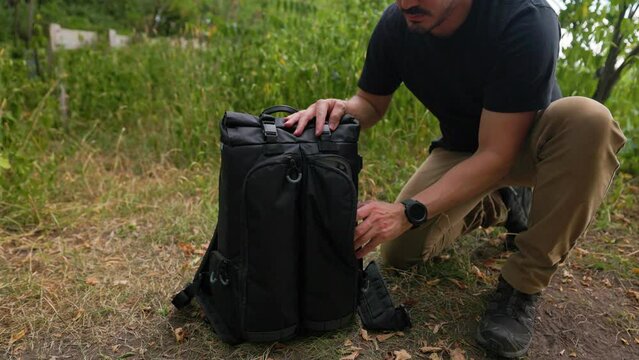 Male photographer reaches into camera bag pulls out drone photography equipment outdoors in a forest setting