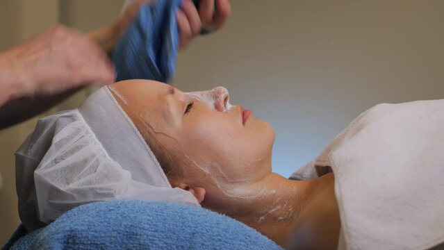 Profile portrait of relaxed woman's face, cosmetologist removes skincare product