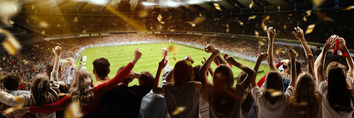 Back view of football, soccer fans cheering their team with flag and posotove emotions at crowded stadium at evening time. Concept of sport, hobby, leisure time, football - obrazy, fototapety, plakaty