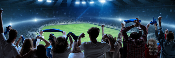 Back view of football, soccer fans cheering their team, holding flag at crowded stadium at evening time. Burst of emotions. Concept of sport, hobby, leisure time, football © master1305