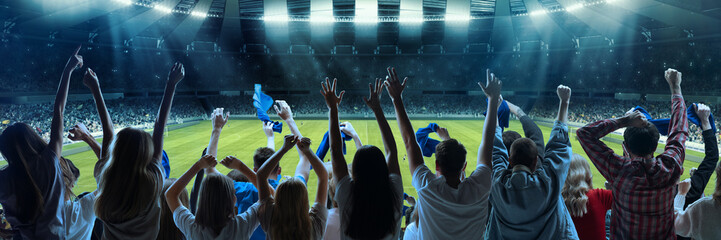 Back view of football, soccer fans emotionally cheering their team at crowded stadium at evening time. Diverse group. Concept of sport, hobby, leisure time, football