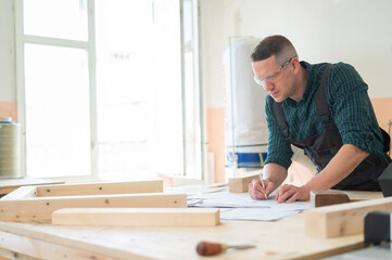 A portrait of a carpenter in goggles and work overalls draws a blueprint for a workshop.