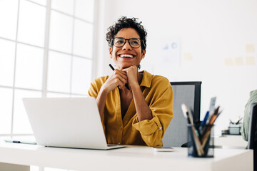 Happy graphics designer sitting at her desk thinking about a design