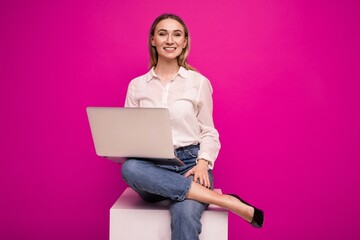 Young woman in a white shirt making a video call from a laptop on a pink background