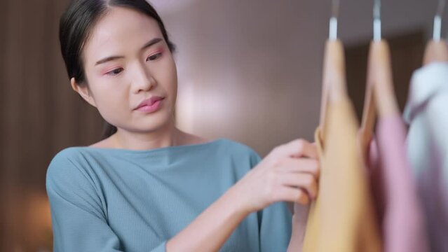 attractive asia adult Young Woman Choosing and arranging clean fresh Dress cloth laundry From hanger at home,portrait asian woman hand moving cloth on hanger laundry housewife at home
