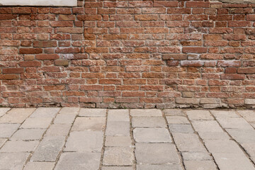Old red brick clay wall with on a sunny day with a walking side pavement. Clay brick walls of Italy. Italian architecture and heritage