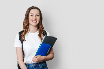 female student with backpack smiles and holds a notebook, copybook, folder in the hands isolated on dark white background