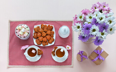 Festive treat with homemade heart-shaped cookies on checkered napkin, bouquet of fresh flowers and gifts in holiday boxes. Celebration of Valentine's Day, anniversary or birthday. Flat lay, mock up