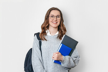 student girl with backpack smiles and holds a notebook, copybook, folder on a white background