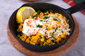 Esquites, grilled corn, served with grated cheese, sour cream, chili powder and slice of lemon in cast iron pan. Mexican street food meal