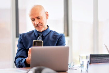 Middle aged businessman sitting at the office and and working and using smartphone and laptop for work