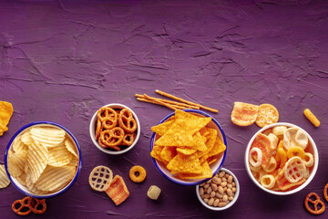 Fototapeta na wymiar Salty snacks with a place for text. Party food. Potato chips, nachos, crackers and other appetizers in bowls, shot from the top
