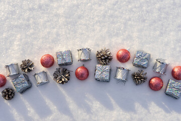 Merry Christmas and Happy New Year. New year toys lying on fresh white sparkling snow on sunny winter day. Silver gifts and drums, pine cones, pink balls. Merry Christmas concept. Top view copy space