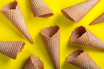 Waffle empty ice cream cones on yellow background, flat lay