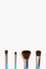A set of four makeup brushes of different shapes on a white background. Four blue makeup brushes in different shapes and sizes. Fashionable women's cosmetics to create beauty. Free space for text