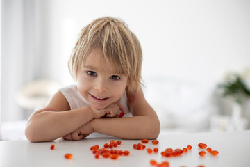 Cute little child, toddler boy, eating alfa omega 3 child suplement vitamin pills at home