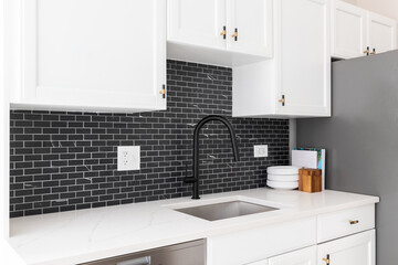 Fototapeta na wymiar Kitchen sink detail shot with white cabinets, small black marble subway tile backsplash, and a black faucet.