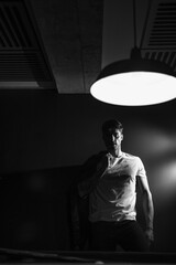 man leaning against wall looking into light, concept photography of handsome man in low light room, black and white photography