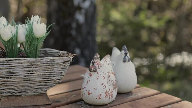 Artificial white tulips and clay chicken on a wooden table