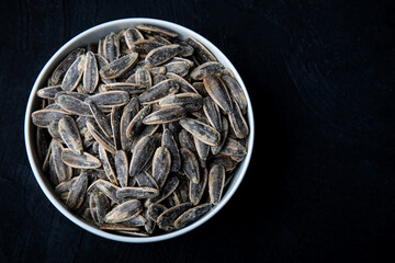 Salty Sunflower crack seeds. Sunflower seeds in white bowl on black background. Salted sunflower seeds in bowl. Close-up.