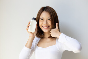 Happy and healthy asian young woman showing thumb up gesture, holding a bottle of fresh and raw wholesome milk