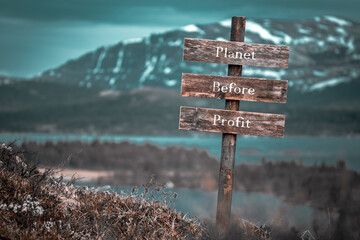 planet before profit text quote engraved on wooden signpost outdoors in landscape looking polluted and apocalyptic.