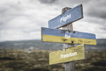 fight for freedom text on wooden signpost with the ukranian flag painted on it. Peace and war concept.