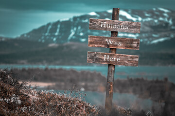 humans was here text quote engraved on wooden signpost outdoors in landscape looking polluted and apocalyptic.
