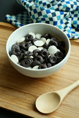 pouring milk into chocolate cereal corn flakes in a bowl on table 