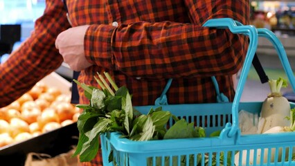 Man picks up an onion from shelf and puts it in shopping basket at grocery store. Buying vegetables at local farmers market. Eating lots onions and vegetables. Buying fresh onions and herbs at market