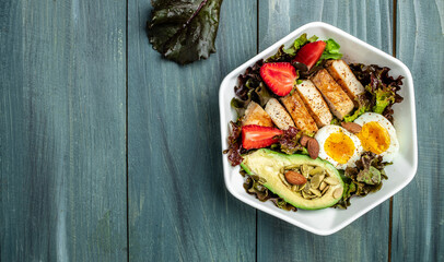 Plate with eggs, bacon, avocado, strawberries and fresh salad on a dark background. Ketogenic diet food, healthy meal concept, Long banner format. top view