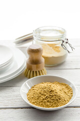 Washing the dishes with mustard powder concept. White clean plates with bowl and jar of yellow...