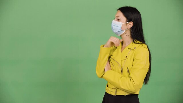 A young beautiful Caucasian woman in a face mask thinks about something - green screen studio